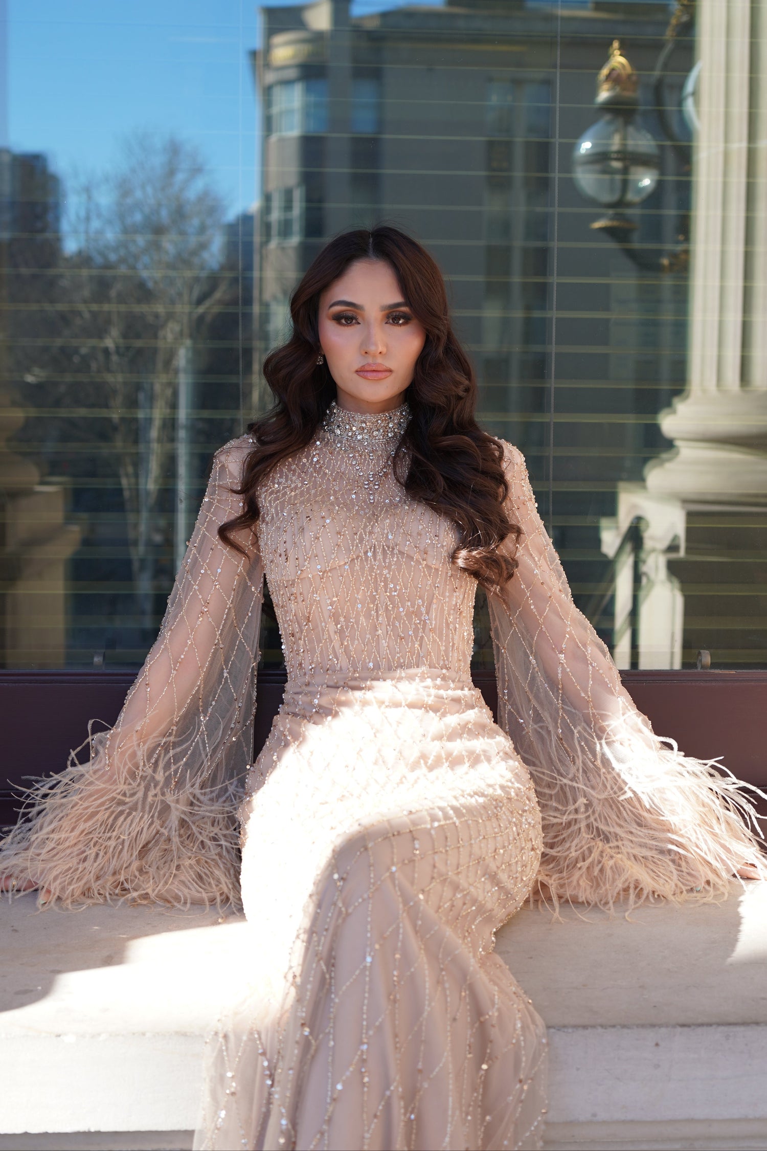 Woman in a beige dress standing in front of a reflective glass building.
